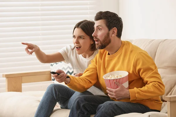 感情的なカップル見ますテレビとともにポップコーンオンソファ — ストック写真