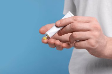 Adam açık mavi arka planda eline tüpten sarı merhem sürüyor, yakın plan. Metin için boşluk