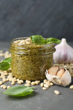 Kavanoz dolusu lezzetli pesto sosu ve malzemeler gri masada, yakın plan.