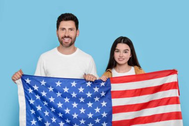 4 Temmuz - ABD 'nin Bağımsızlık Günü. Mutlu adam ve kızı açık mavi arka planda Amerikan bayrağı taşıyorlar.
