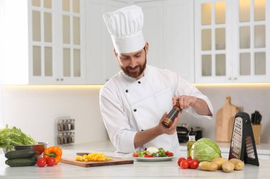 Profesyonel şef mutfaktaki mermer masada lezzetli salataya biber ekliyor.