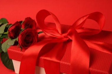 Kırmızı arka planda fiyonklu ve güllü güzel hediye kutusu, yakın plan.