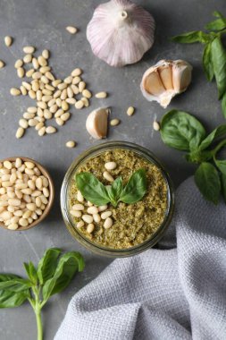 Lezzetli pesto sosu kavanozu ve gri masadaki malzemeler düz.