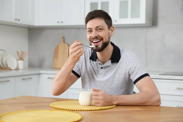 一个英俊的男人在厨房的桌子上吃着美味的酸奶 — 图库照片