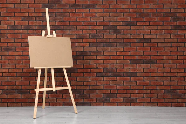 stock image Wooden easel with blank board near brick wall indoors. Space for text