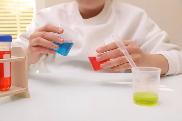 女孩把五颜六色的液体混合在室内的白桌上 儿童化学实验集 — 图库照片