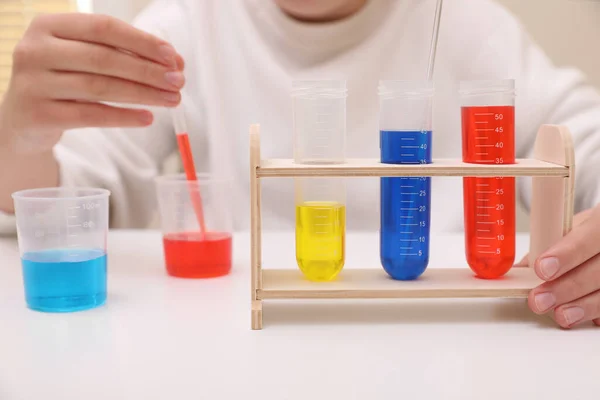 女孩把五颜六色的液体混合在室内的白桌上 儿童化学实验集 — 图库照片