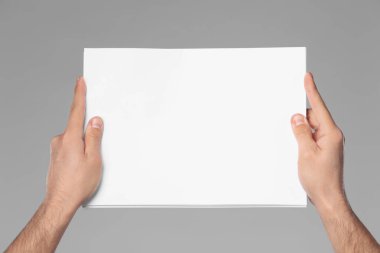 Man holding sheet of paper on grey background, closeup. Mockup for design