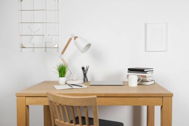 Evdeki ahşap masada dizüstü bilgisayarı, lambası ve kırtasiyesi olan rahat çalışma alanı.