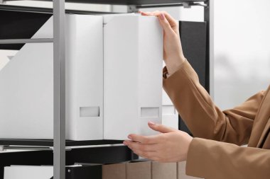 Woman taking folder with documents from shelf in office, closeup