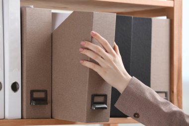 Woman taking folder with documents from shelf in office, closeup