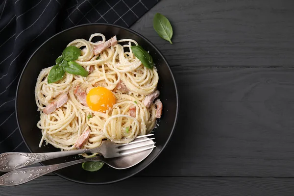 Yumurta sarısı ve çatal bıçaklı Carbonara makarnası siyah ahşap masada, düz yerde. Metin için boşluk