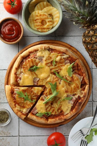 Delicious cut pineapple pizza and ingredients on light gray tiled table, flat lay
