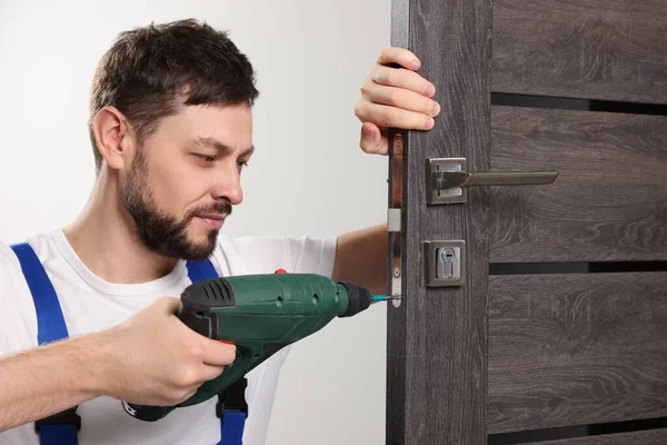 Worker with screw gun repairing door lock indoors