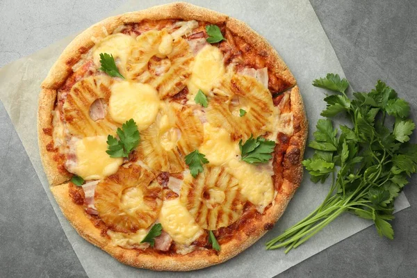 Delicious pineapple pizza and parsley on gray table, top view