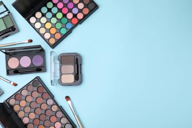 Açık mavi arka planda güzel göz farı paletleri ve fırçaları olan düz bir kompozisyon. Metin için boşluk