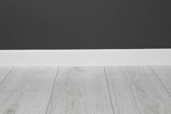 Белый плинтус на ламинированном полу возле черной стены в помещении