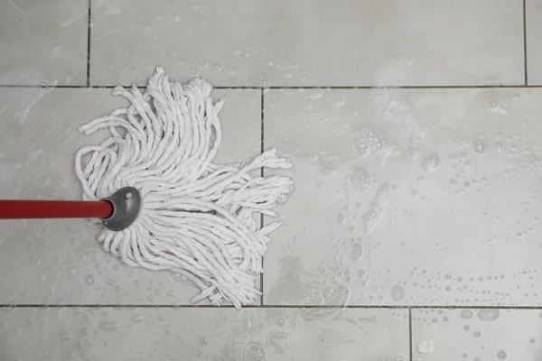 Cleaning grey tiled floor with string mop, top view. Space for text