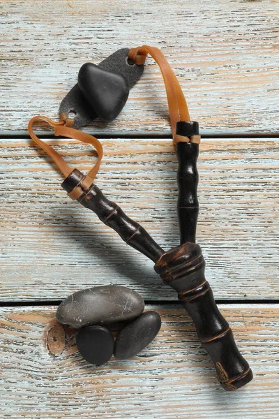 stock image Black slingshot with stones on old light blue wooden table, flat lay