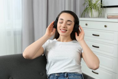 Kulaklıklı mutlu kadın evdeki yumuşak koltukta müzik dinliyor.