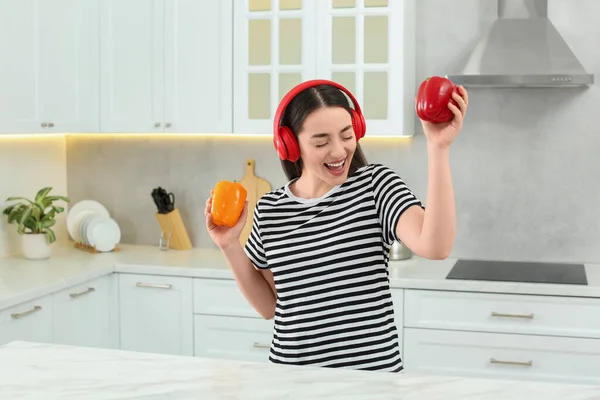 stock image Happy woman in headphones listening music and dancing with bell peppers in kitchen