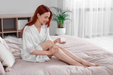 Güzel genç bir kadın yatak odasındaki bacaklara vücut kremi sürüyor.