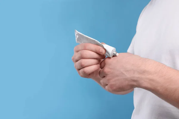 stock image Man applying ointment from tube onto his hand on light blue background, closeup. Space for text