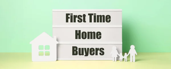 First time home buyers. Lightbox, figures of family and house on table against green wall. Banner design