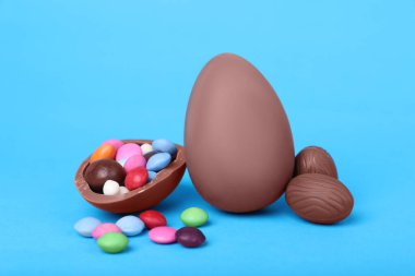 Delicious chocolate eggs and candies on light blue background, closeup clipart