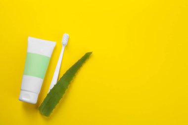 Aloe vera diş macunu boş tüpte, fırça ve yeşil yaprak sarı arka planda, düz yerde. Metin için boşluk