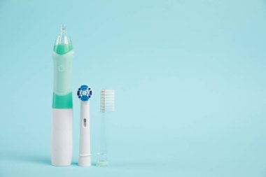 Açık mavi arkaplanda elektrikli diş fırçası ve yedek fırça başlıkları, metin için boşluk