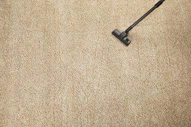 Modern elektrikli süpürgeyle bej halıları süpürüyor. Metin için boşluk