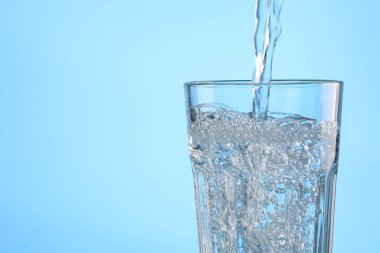 Açık mavi arka planda bardağa su dökmek, yakın plan. Metin için boşluk