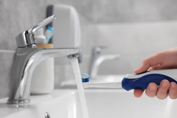 電気歯ブラシを持っている女性は バスルームでシンクの上に流れる水の近くにペースト クローズアップ — ストック写真