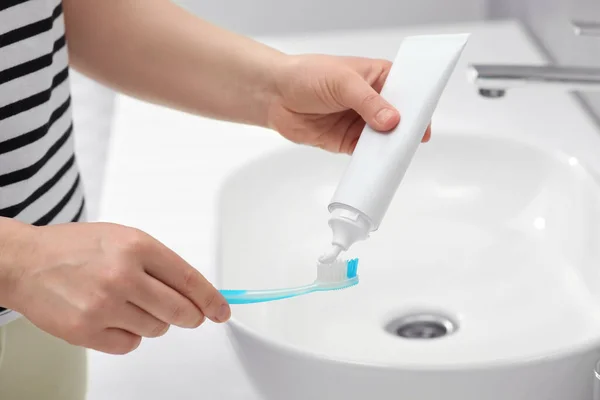バスルームのシンクの近くの歯ブラシにチューブから歯磨き粉を絞る女性 クローズアップ — ストック写真