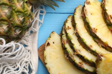Açık mavi ahşap masa üzerinde olgun ananas dilimleri, düz uzanmış