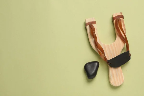 stock image Wooden slingshot with pebble on olive background, top view. Space for text