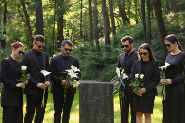 Mezarlıktaki granit mezar taşının yanında çiçek taşıyan üzgün insanlar. Cenaze töreni.