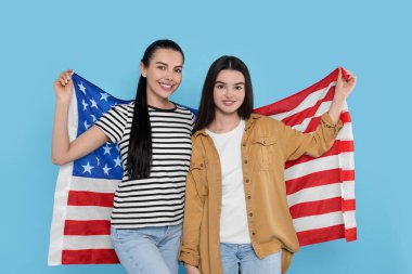 4 Temmuz - ABD 'nin Bağımsızlık Günü. Açık mavi arka planda Amerikan bayrağı taşıyan mutlu kadın ve kızı