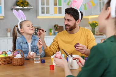 Happy family having fun while painting Easter eggs at table in kitchen