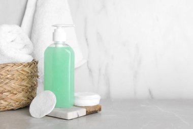 Bir şişe yüz temizleme ürünü, pamuk pedler ve açık gri masada havlu. Metin için boşluk