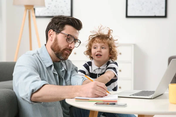 stock image Little boy bothering his father at home. Man working remotely at desk