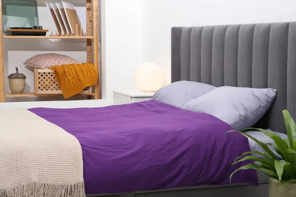 Comfortable bed with purple linens in bedroom. Interior design