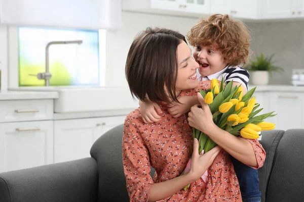 stock image Little son congratulating his mom with Mother`s day at home. Woman holding bouquet of yellow tulips