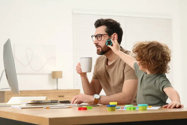 stock image Little boy bothering his father at home. Man working remotely at desk