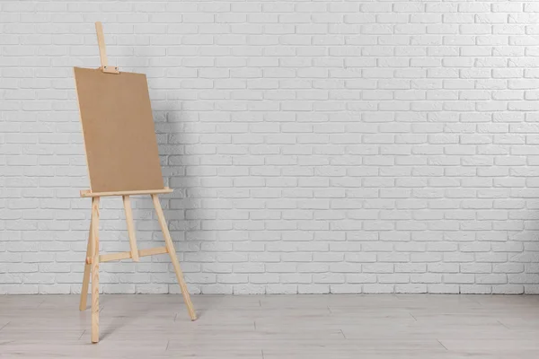 stock image Wooden easel with blank board near white brick wall indoors. Space for text