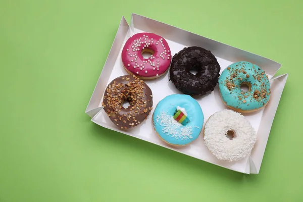 stock image Box with different tasty glazed donuts on light green background, top view