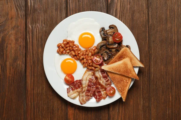 揚げ卵とプレート キノコ トマト ベーコンと木製のテーブルの上にトースト トップビュー 伝統的な英語の朝食 — ストック写真