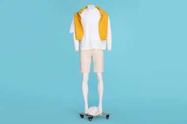 Beyaz tişört, şık şort ve açık mavi arka planda turuncu süveter giyen erkek mankeni.