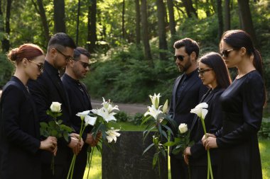 Mezarlıktaki granit mezar taşının yanında çiçek taşıyan üzgün insanlar. Cenaze töreni.